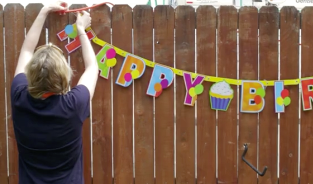 woman hanging happy birthday signage on fence for the Birthday Party Project