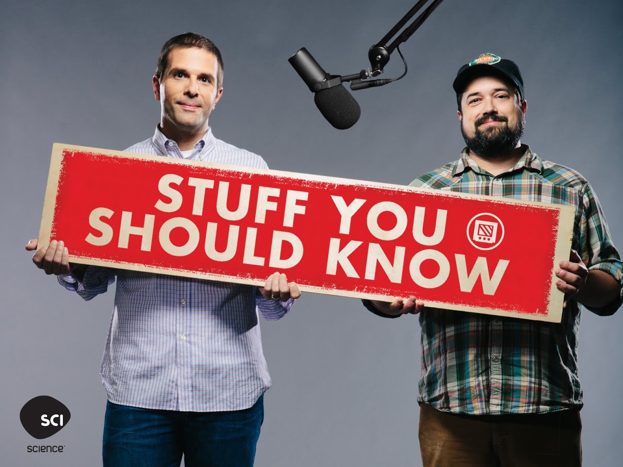 josh and chuck from stuff you should know holding up a sign in front of a mic